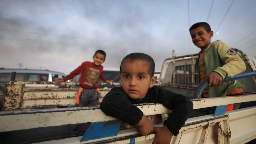 Three boys in the back of a truck looking at the camera as they flee a Syrian town.