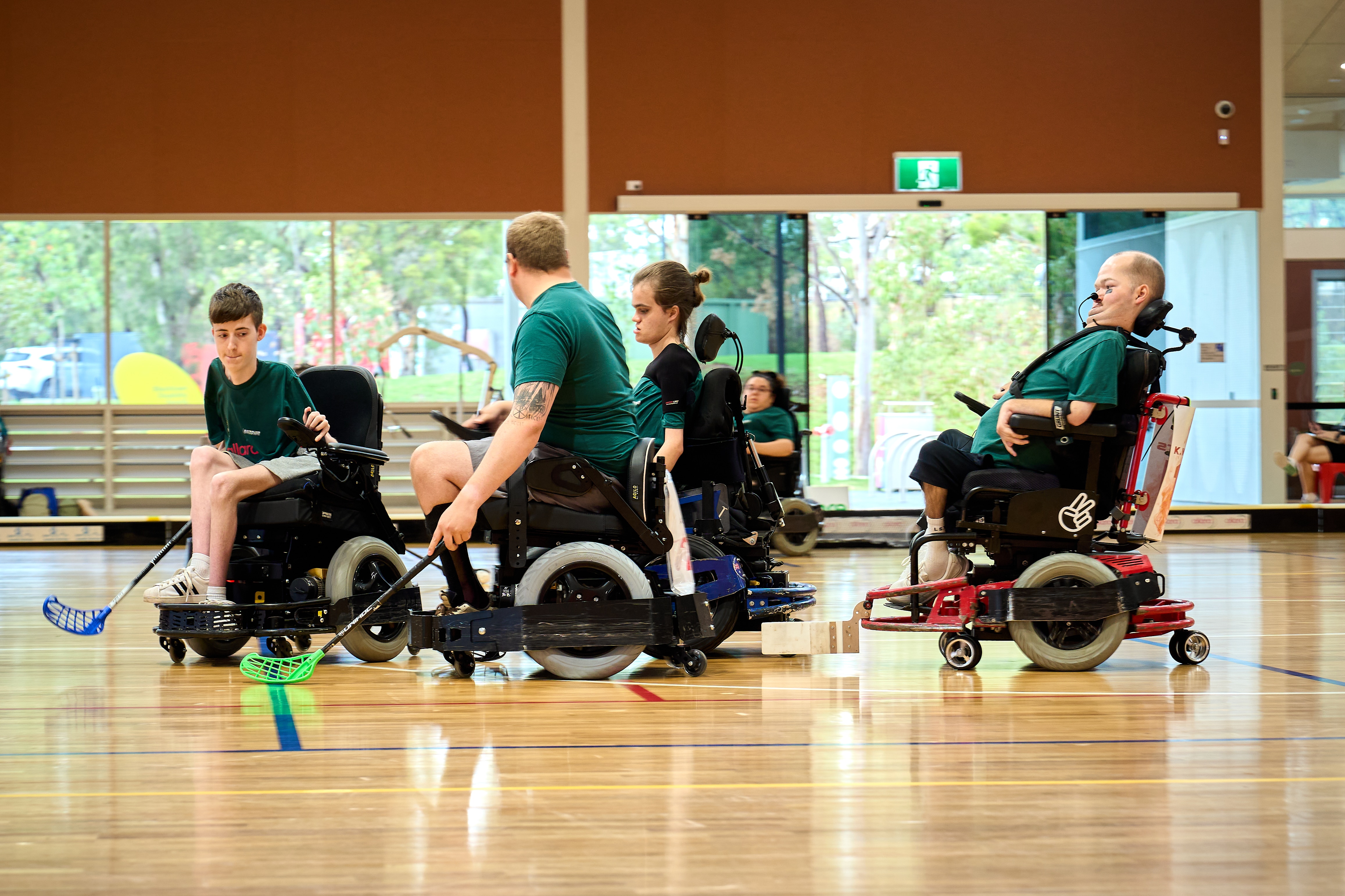 Grupo de jogadores de verde em cadeira de rodas motorizada na quadra segurando bastões