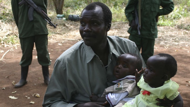 Joseph Kony sits surrounded by soldiers while holding his daughter and son