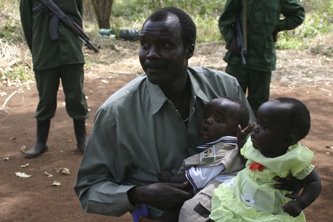 Joseph Kony sits surrounded by soldiers while holding his daughter and son