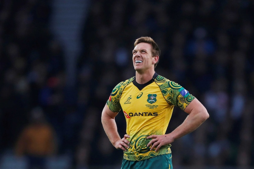 a man in a gold and green jersey grimaces while looking up