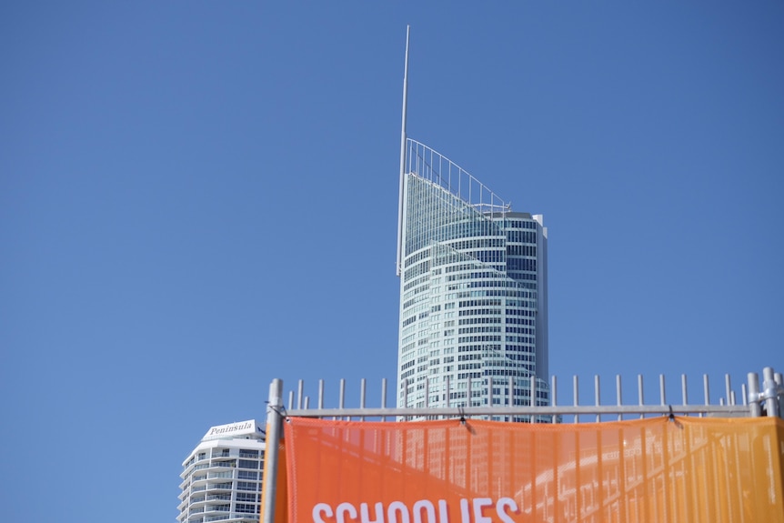 A skyscraper looms behind a "Schoolies" banner.