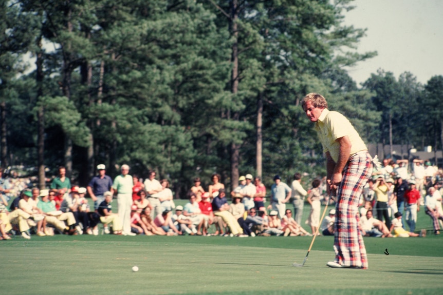 A golfer wearing yellow and red putts during a tournament