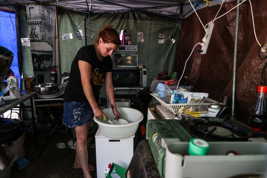 A woman washing a plate in a tub in a tent.