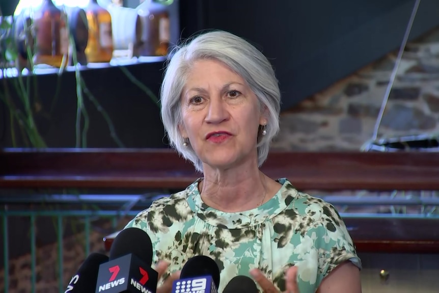 A woman with short grey hair wearing a green floral top