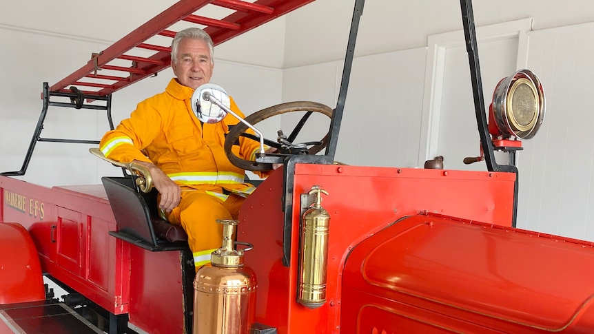 A firefighter sits at the wheel of a red Garford fire truck.