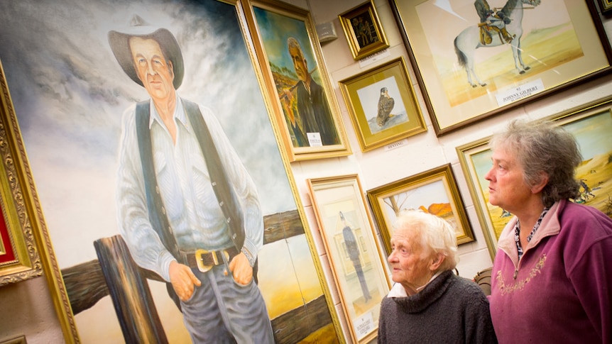 A large painting of Slim Dusty being viewed by Nan and Megan Harding.