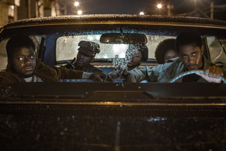Actors Daniel Kaluuya & Lakeith Stanfield sit in the front of a car, more people in the back, in film Judas and the Black Messia