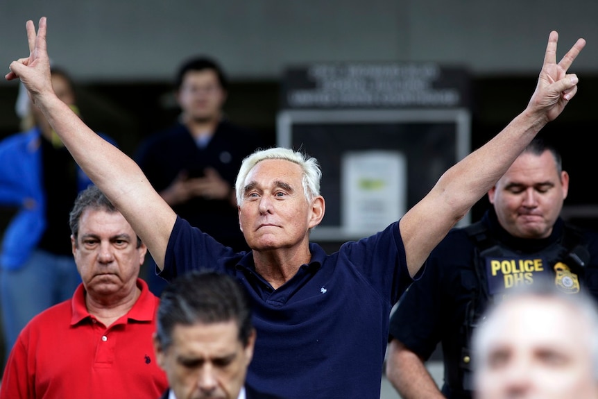 Roger Stone holds his arms up, outstretched, with his fingers making V for victory gestures, as he walks out of a courthouse