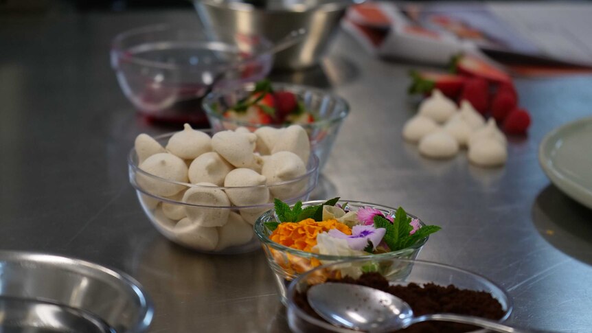 Clear bowls containing decorative flowers and mint leaves, and small meringues and strawberries.