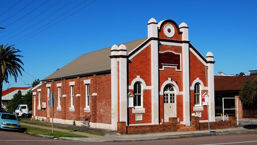 A large red brick building with ornate cream features stands on a corner with bright blue sky above