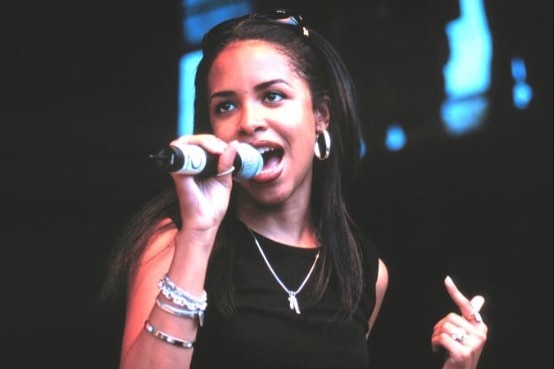 Aaliyah sings into a microphone on stage.