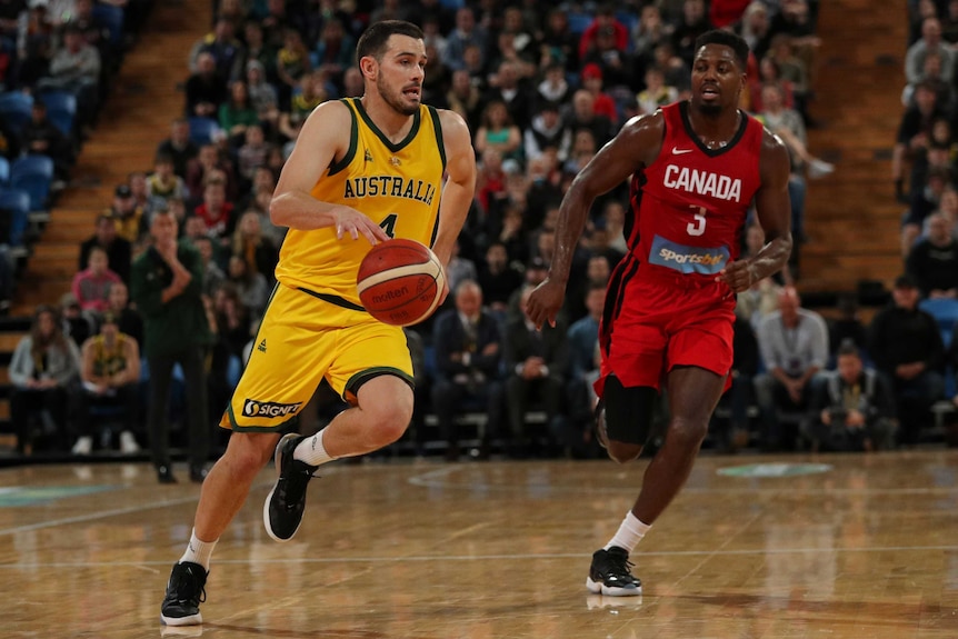 Chris Goulding, wearing a yellow singlet, bounces a basketball and runs past a man in a red singlet