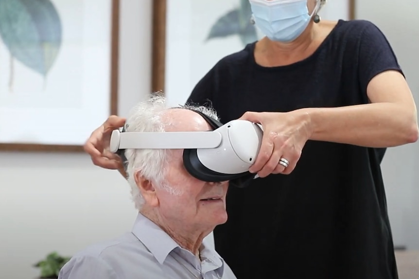An older man has virtual reality glasses put on his face.