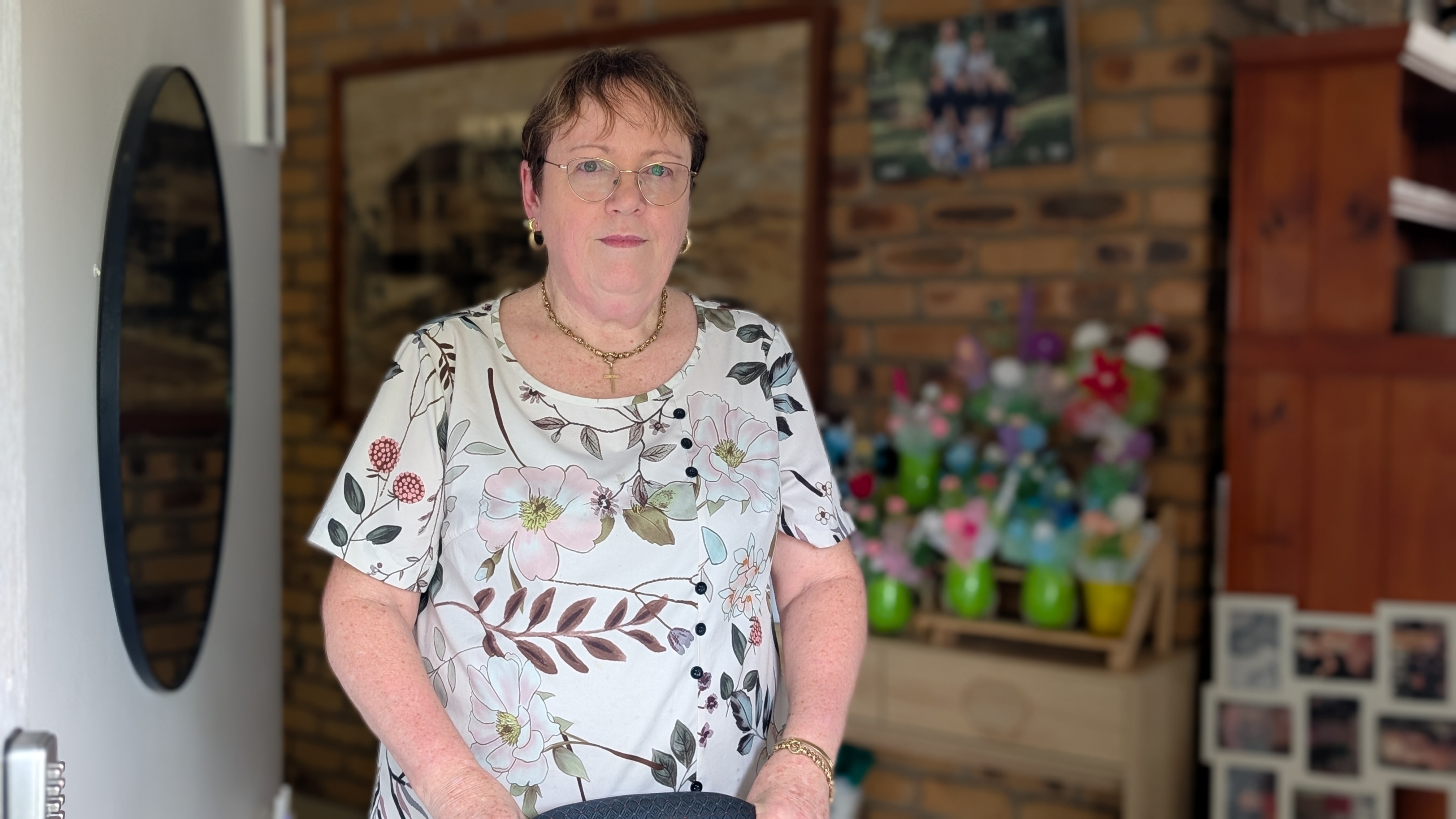 A woman in a floral shirt standing inside a doorway.