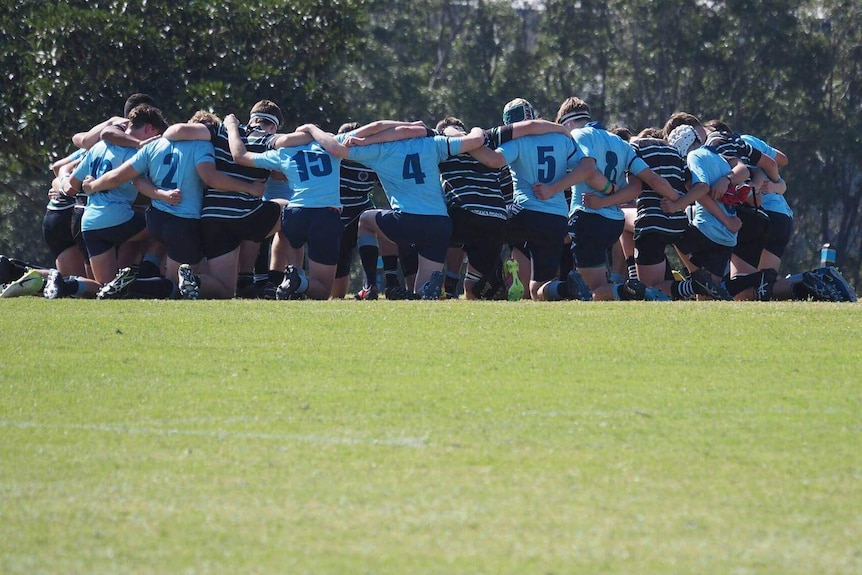 Schoolboy rugby players crouched and arms across one another in prayer