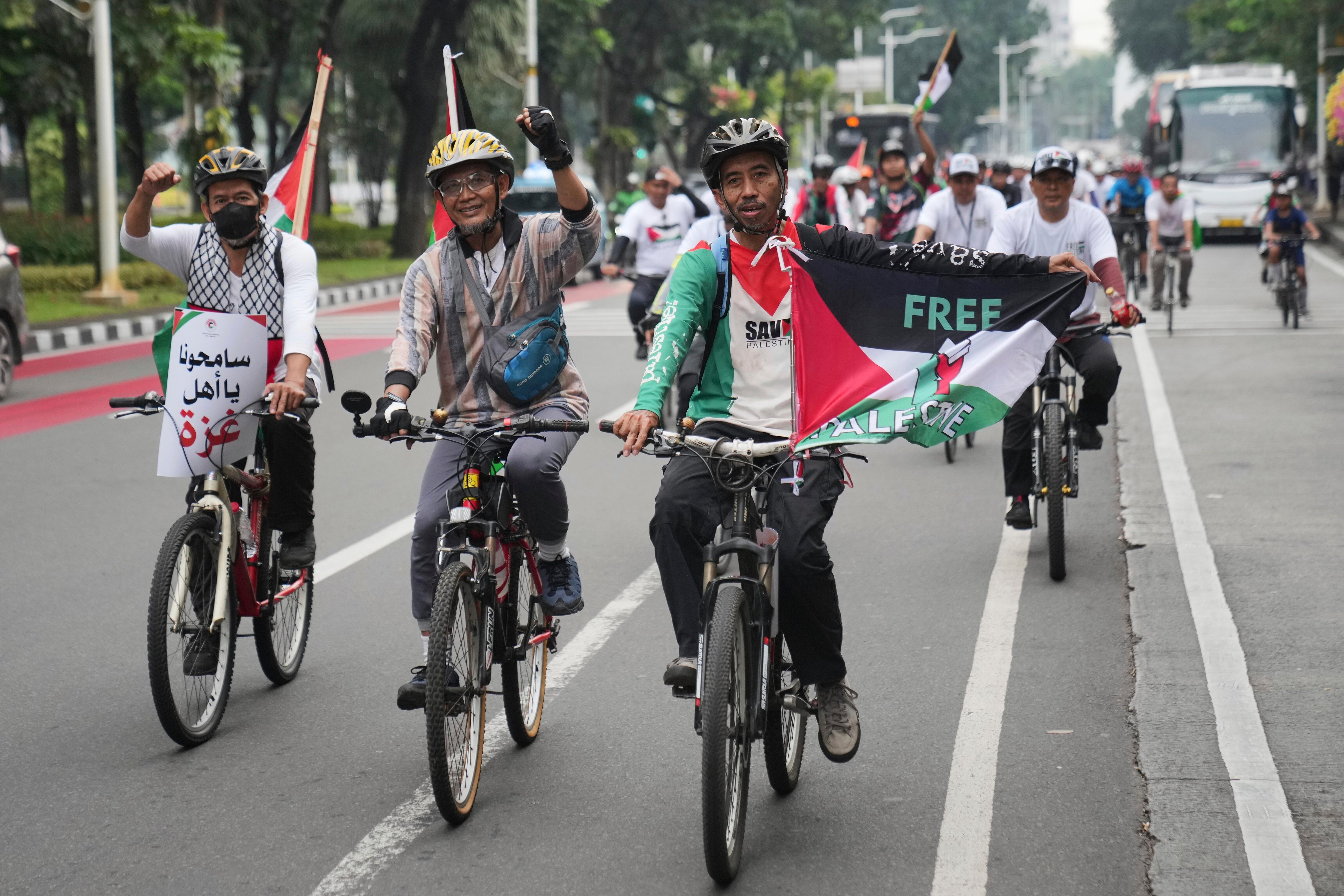 three men with helmets riding bicycles on the road carry a red, black, green and white flag with the words free Palestine 