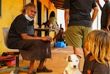 Valerie Martin sits down in the Yuendumu community near a child holding a dog.