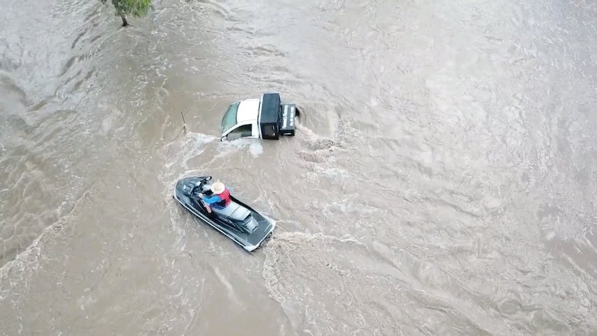  A man is on a jet ski in flood waters and a truck that's covered in water is next to them.