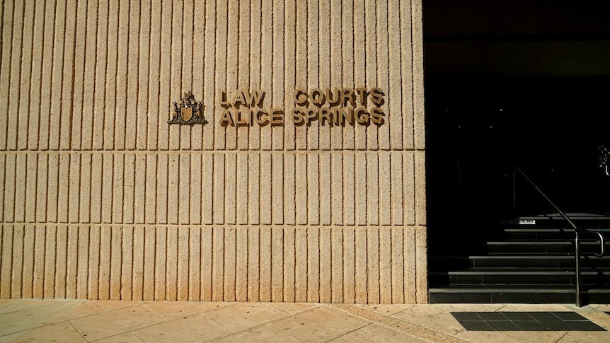 The wall of a brutalist, beige building, with the words 'Law Courts Alice Springs' on the world in bronze.