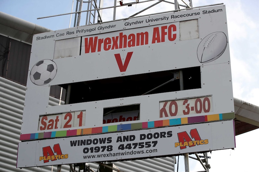 A board shows the details for the next game for football club Wrexham AFC outside the home ground.