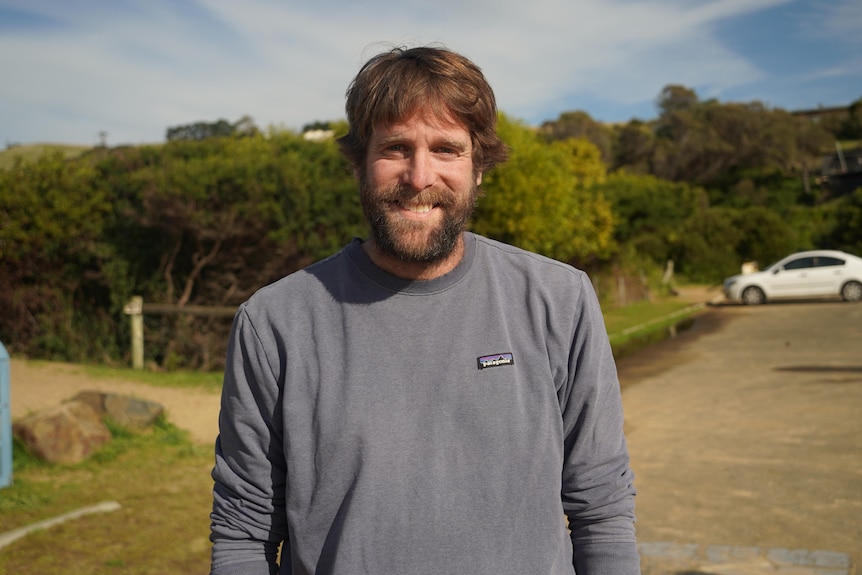 A young bearded man stands in a car park