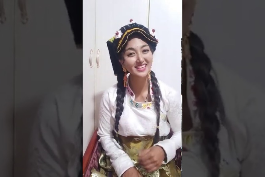 A woman in traditional Tibetan attire smiles while doing a livestream