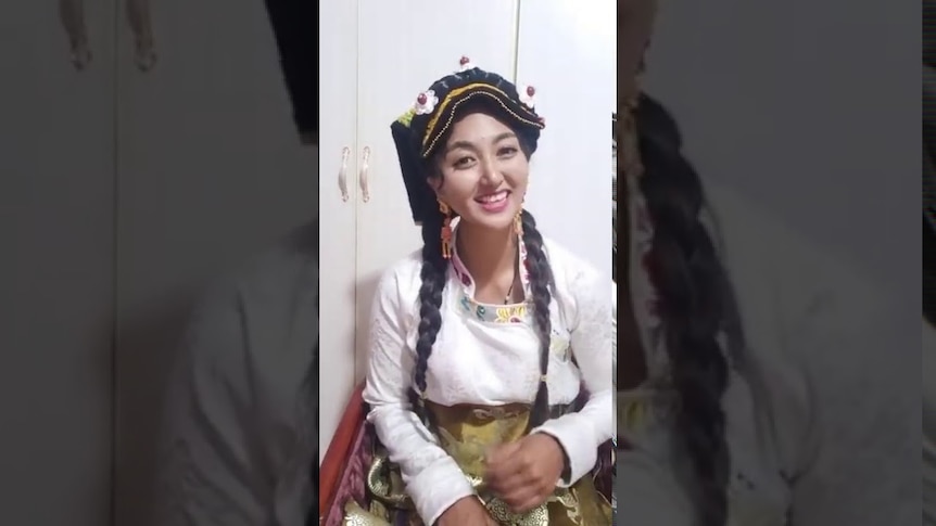 A woman in traditional Tibetan attire smiles while doing a livestream