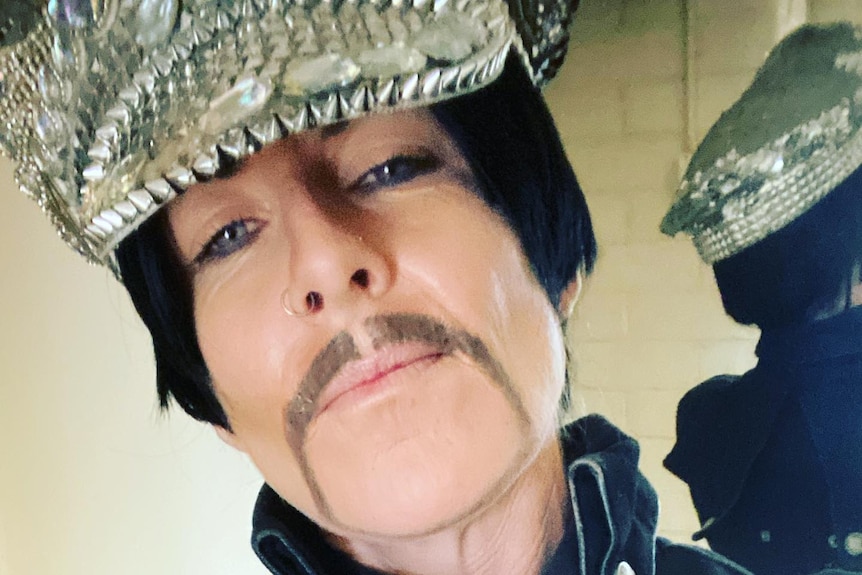 A drag king with a moustache wearing a bejeweled cap.