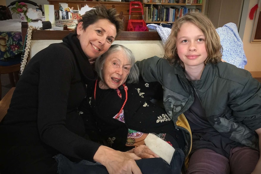 Three family members sit hugging in a couch.