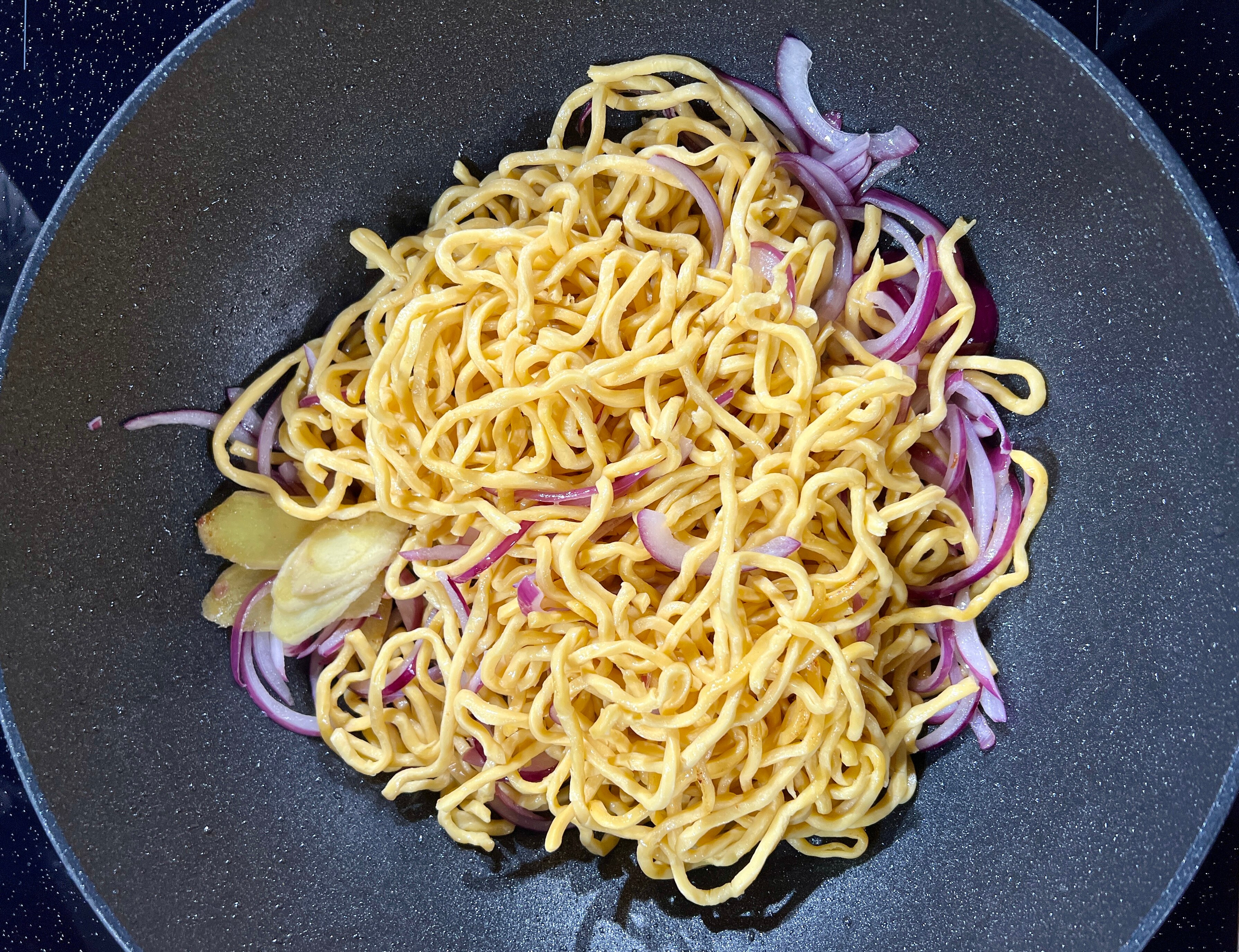 팬에 담긴 호키엔 국수와 얇게 썬 붉은 양파, 생강 사진