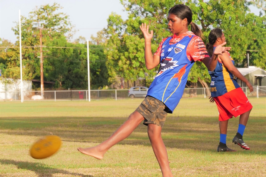 A young girl kicks a football at training in Barunga.