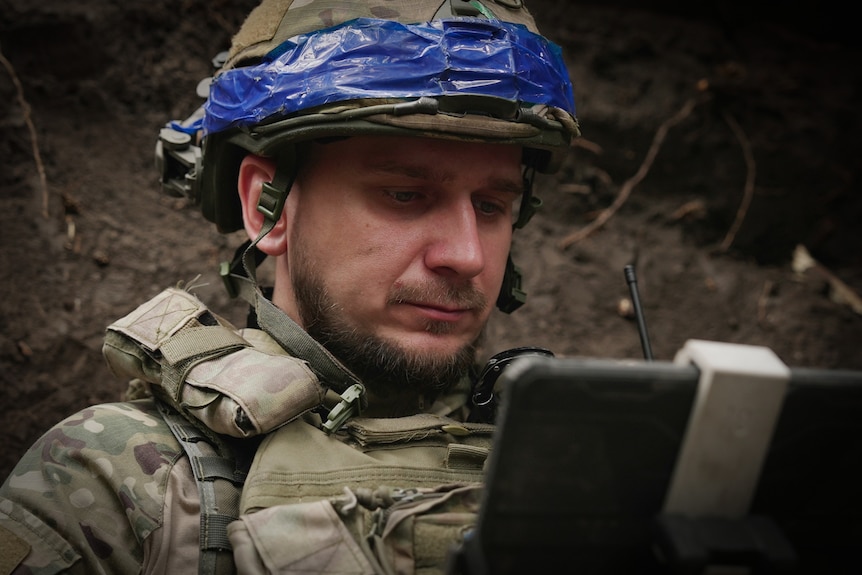 A man wearing a helmet and camouflage gear looks at his laptop.