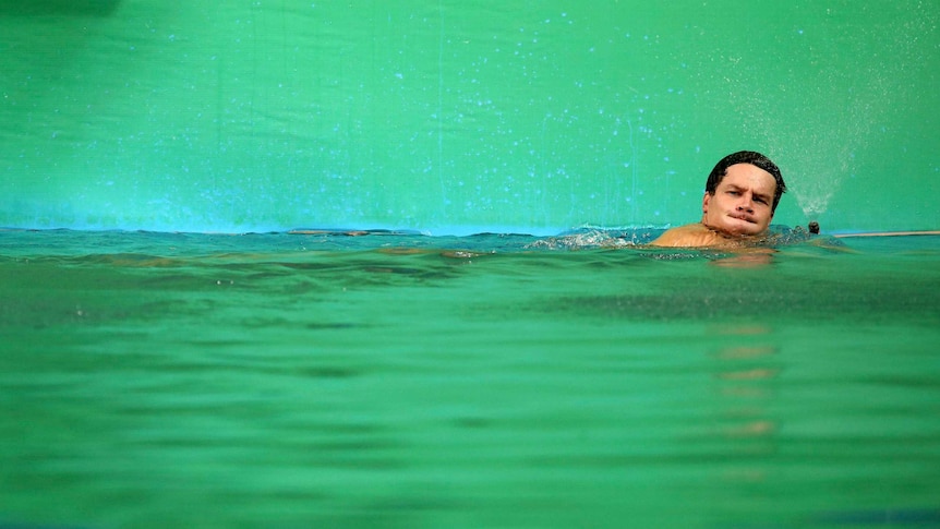A German athlete takes a breath while swimming in a bright green pool.