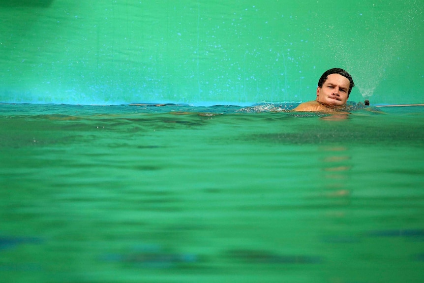 A German athlete takes a breath while swimming in a bright green pool.