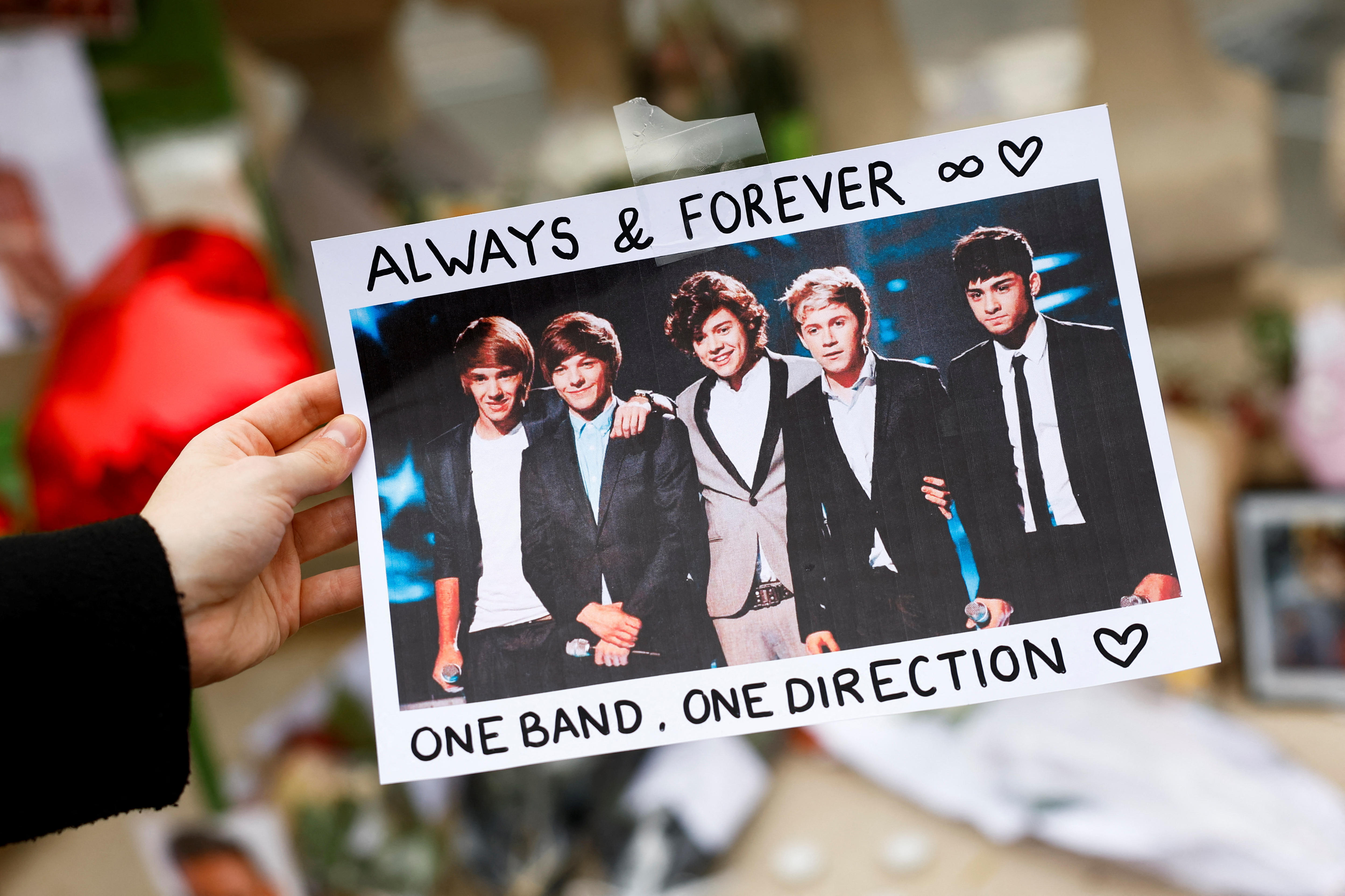 A person holds a poster with an image of One Direction band members with "always and forever" written on it