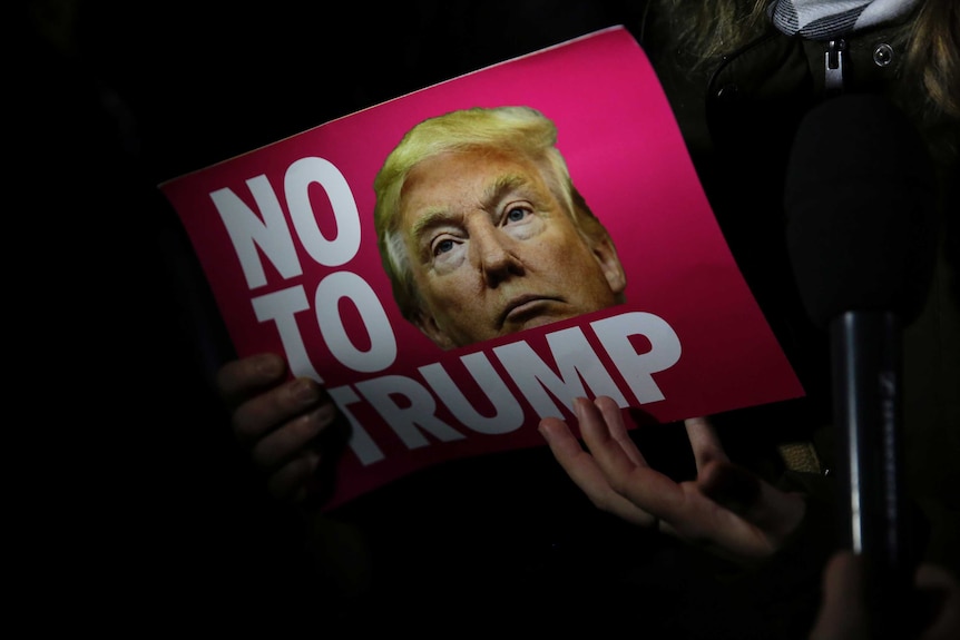 A woman holds a 'No Trump' placard
