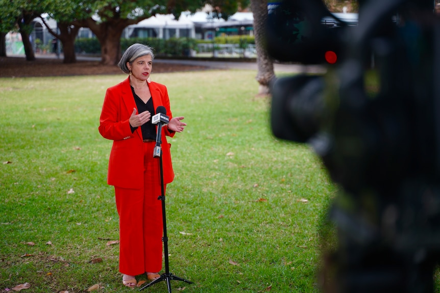 A woman wearing a bright orange suit in a park being interviewed by ABC news