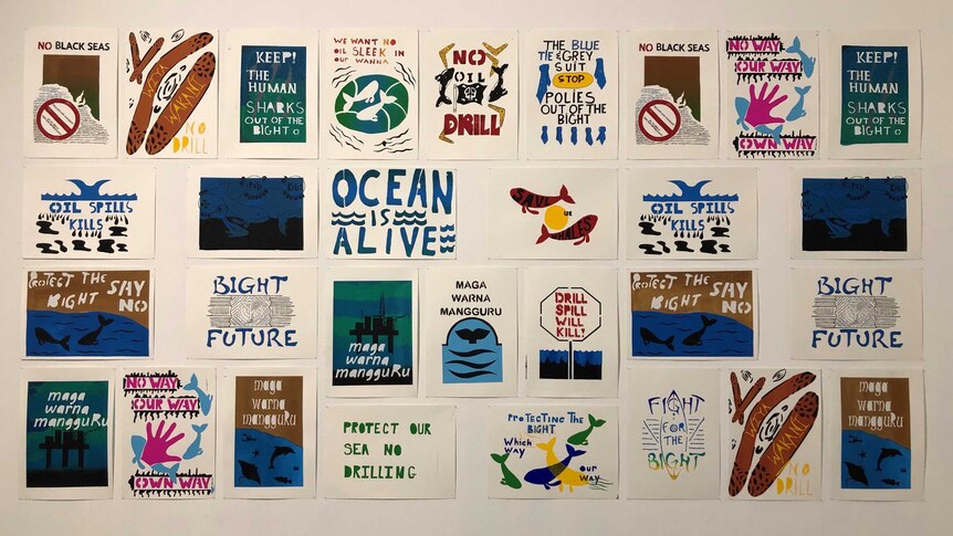 20 prints adorn a white wall with various slogans such as 'ocean is alive' and 'oil spill kills'
