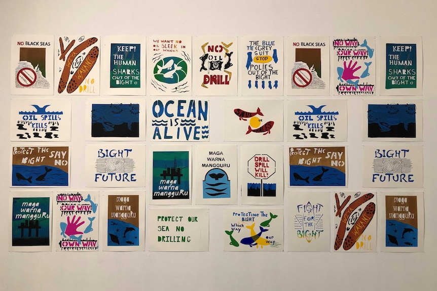 20 prints adorn a white wall with various slogans such as 'ocean is alive' and 'oil spill kills'