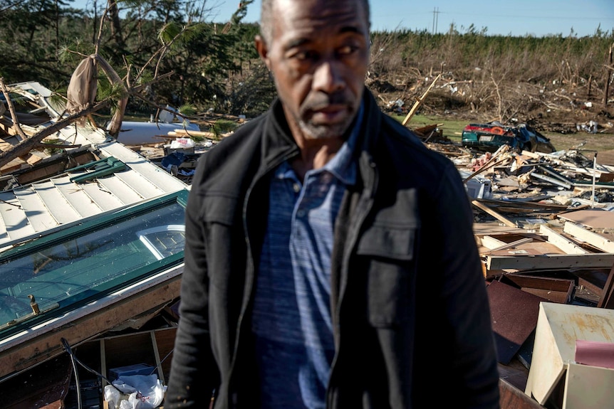A man stands in front of a pile of rubble.