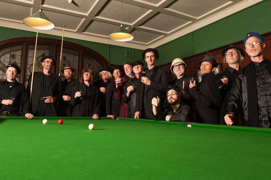 A group of 14 men stand behind a pool table. 