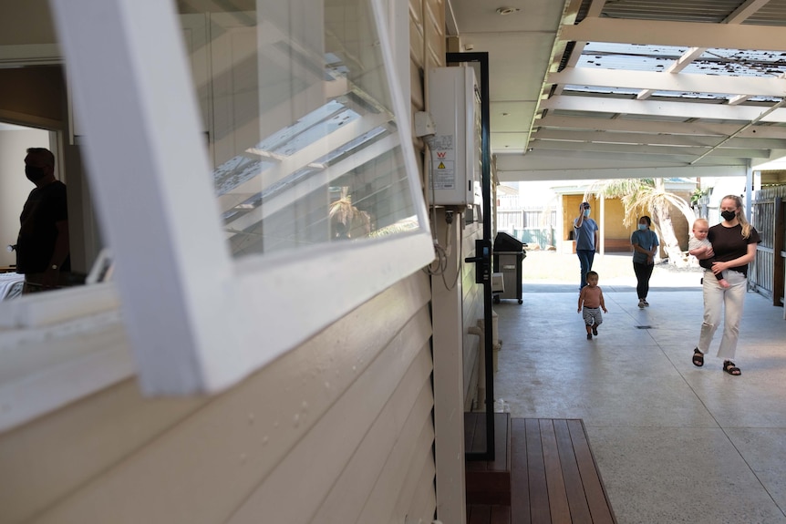 A family walk through an open home in the back covered driveway. 