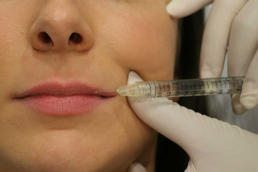 A close-up shot of a woman's face with a needle held to her lips.