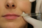 A close-up shot of a woman's face with a needle held to her lips.