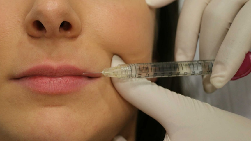 A close-up shot of a woman's face with a needle held to her lips.