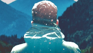 The back of a man's head as he stares at a mountain range.