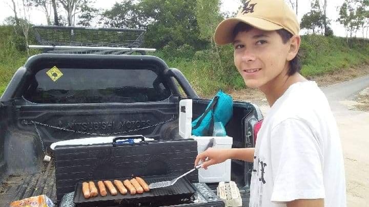 a teenage boy cooks sausages on a barbecue and looks at the camera