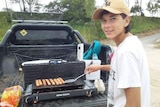 a teenage boy cooks sausages on a barbecue and looks at the camera
