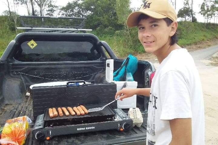 a teenage boy cooks sausages on a barbecue and looks at the camera